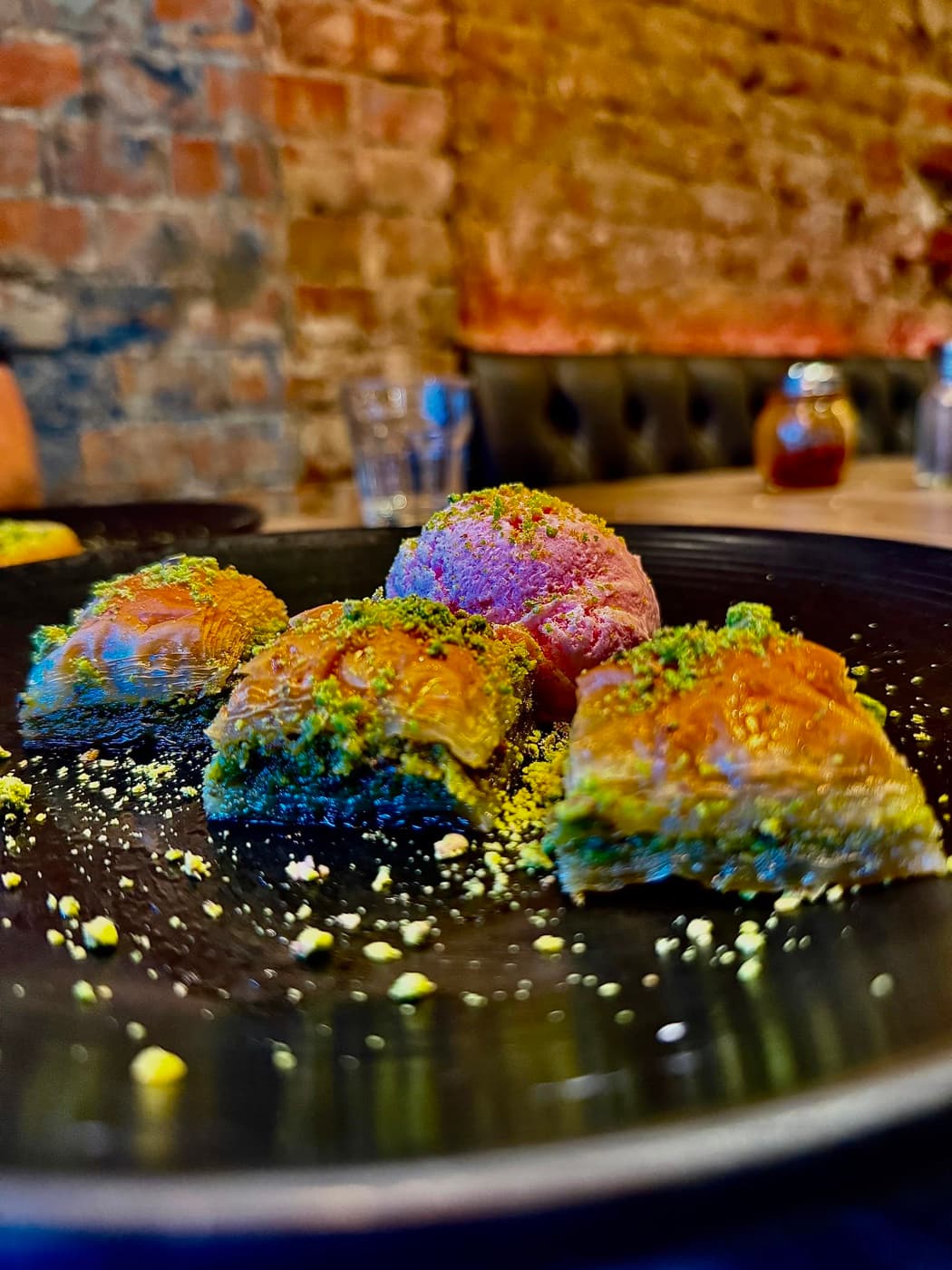Baklava at Antep Kitchen Oxford, dusted with crushed pistachio and served with a scoop of ice cream on a black plate
